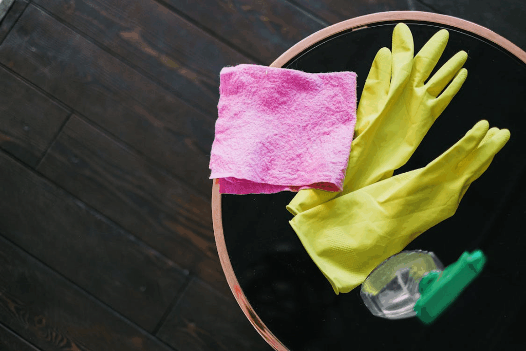An image of cleaning supplies including latex gloves, spray, and a microfiber cloth resting on a coffee table.