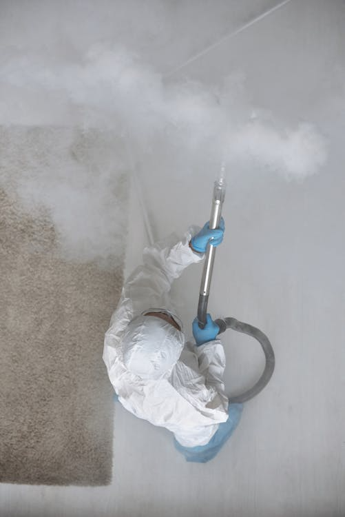 A person wearing white safety clothes, using an advanced tool to fumigate a room.